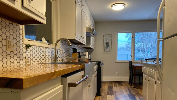 A kitchen with white cabinets, a wooden countertop, and a view of the outdoors through a window. - Cozy 3-bedroom house in Anchorage (Anchorage)