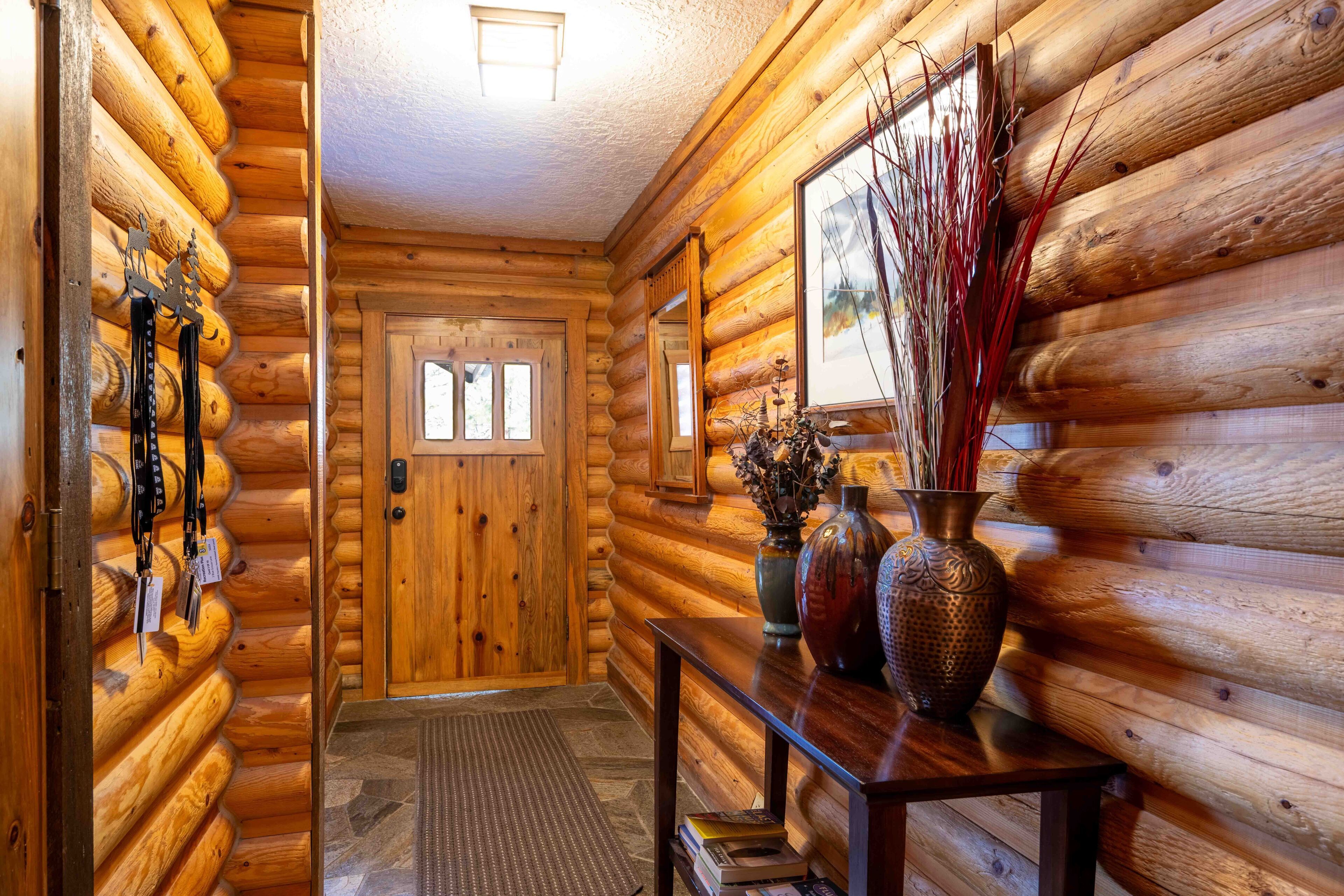 A log cabin interior with a wooden door, a console table with vases, and a ski rack.
