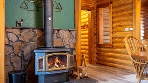 A log cabin interior with a stone fireplace, wooden walls, and a dining area. - The Log Cabin Where Memories are Made (Sunriver)