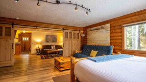 A cozy log cabin room with a large bed, a wooden bench, and a dining table. - The Log Cabin Where Memories are Made (Sunriver)