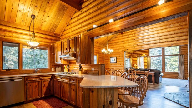 A log cabin interior with a kitchen, dining area, and large windows. - The Log Cabin Where Memories are Made (Sunriver)