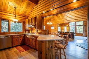 L’intérieur d’une cabane en rondins comprend une cuisine, un coin repas et de grandes fenêtres.