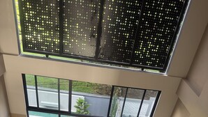 Un interior moderno con ventanas amplias, un banco de madera, plantas en macetas y una lámpara de escritorio negra.