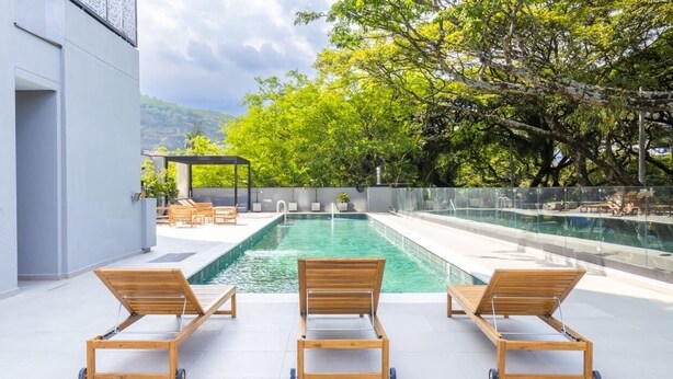 A pool area with three wooden loungers, a pergola, and a view of trees and hills. - Cozy 1-bedroom apartment with AC in tranquil Cali (Cali)