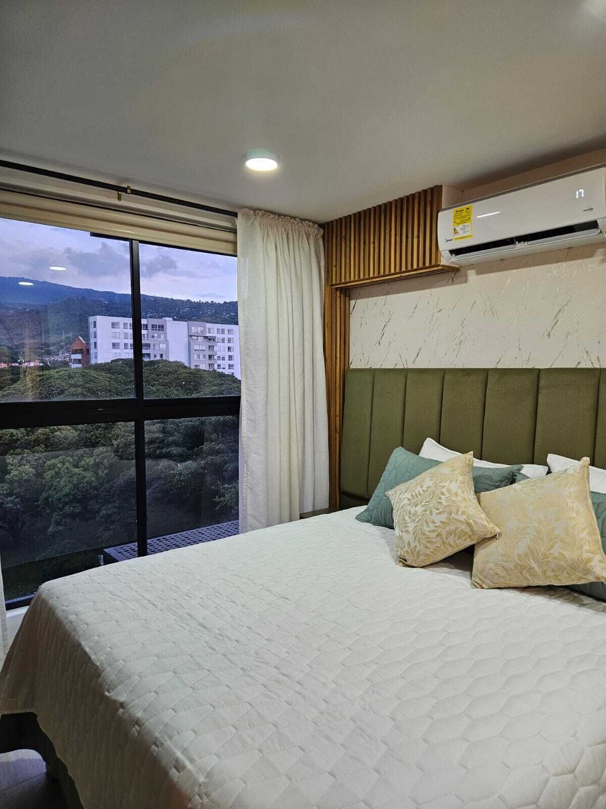 Une chambre d’hôtel avec un grand lit, une vue sur les bâtiments et la verdure, et un appareil de climatisation.