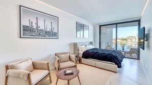 A modern bedroom with a bed, two armchairs, a coffee table, and artwork on the wall. - Beautiful New Luxury Apartment - Cora Sunset at Campestre (San Jose Del Cabo)