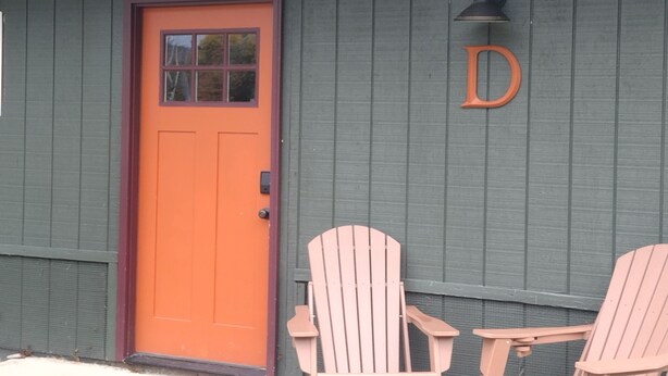 Une porte en bois avec un cadre rouge, une petite fenêtre et une lettre « D » fixée au mur.