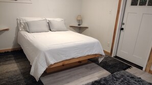 Une chambre à coucher avec un lit, une table de chevet, une lampe et une porte.