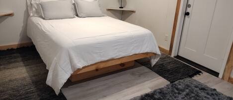 Un dormitorio con cama, mesita de noche, lámpara y puerta.