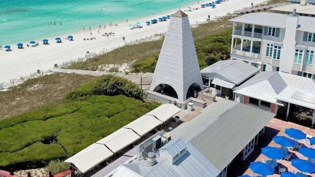 A beachfront hotel with a distinctive pyramid-shaped building, a sandy beach with umbrellas, and a clear view of the ocean.