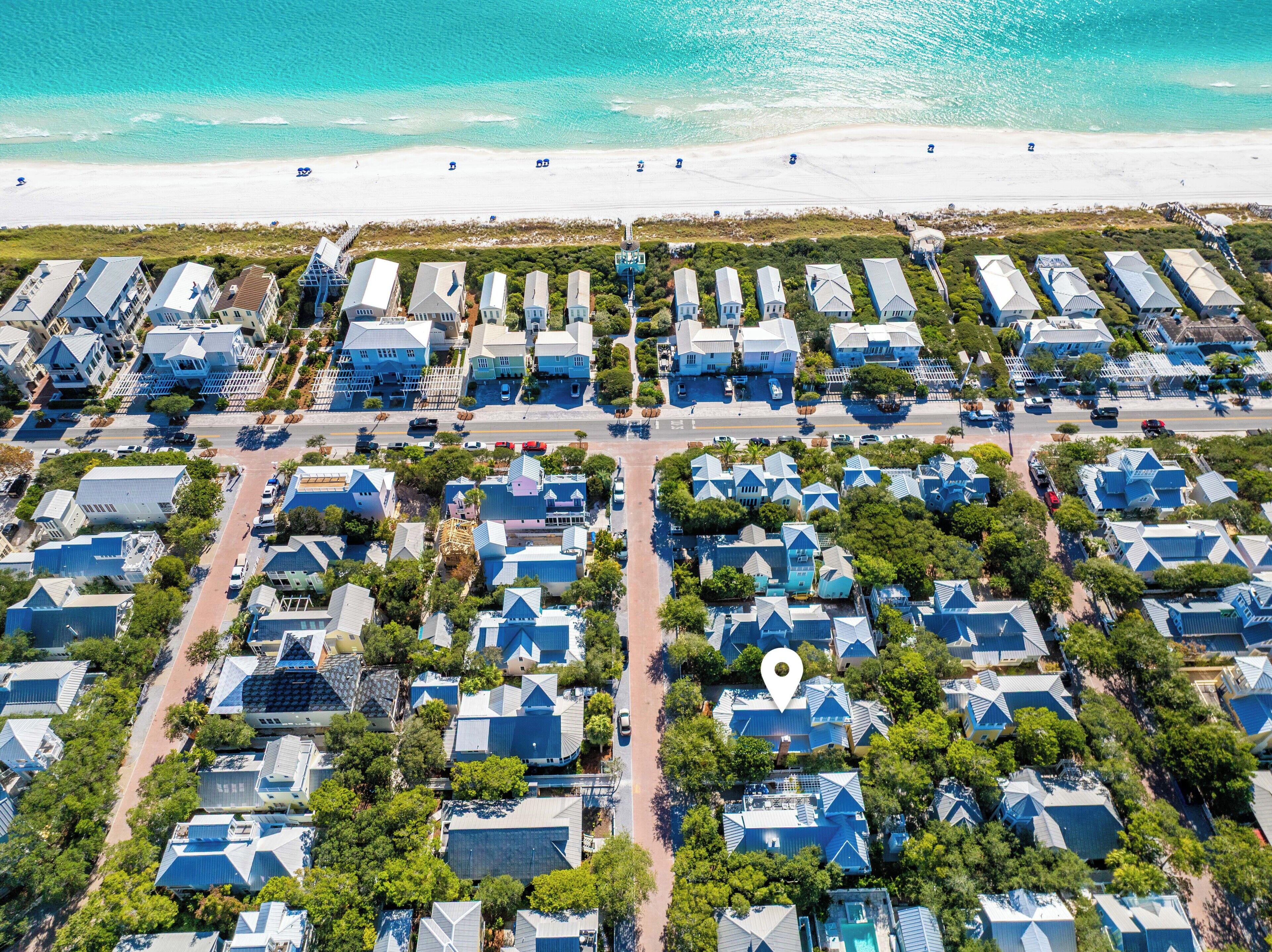 Vue aérienne d’un quartier résidentiel situé sur la côte, avec des maisons aux toits bleus de couleur uniforme, une plage en arrière-plan et un réseau routier bien défini.