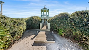 A wooden pathway leading to a gazebo with a statue on top, surrounded by dense foliage.