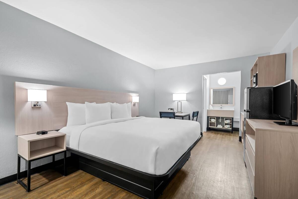 Ein modernes Hotelzimmer mit einem großen Bett, Nachttischen, einem Schreibtisch, einem Fernseher und einem Badebereich.