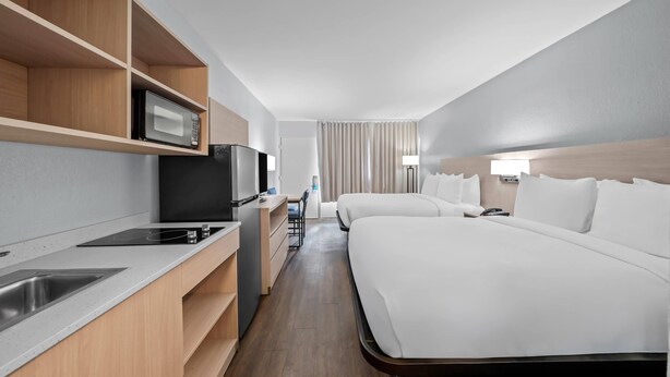 A hotel room with a kitchenette, a bed, a desk, and a TV. - Suburban Studios Daytona Beach - Speedway (Daytona Beach)