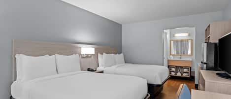 Habitación de hotel con dos camas, un escritorio, un televisor y un baño visible a través de una puerta abierta.