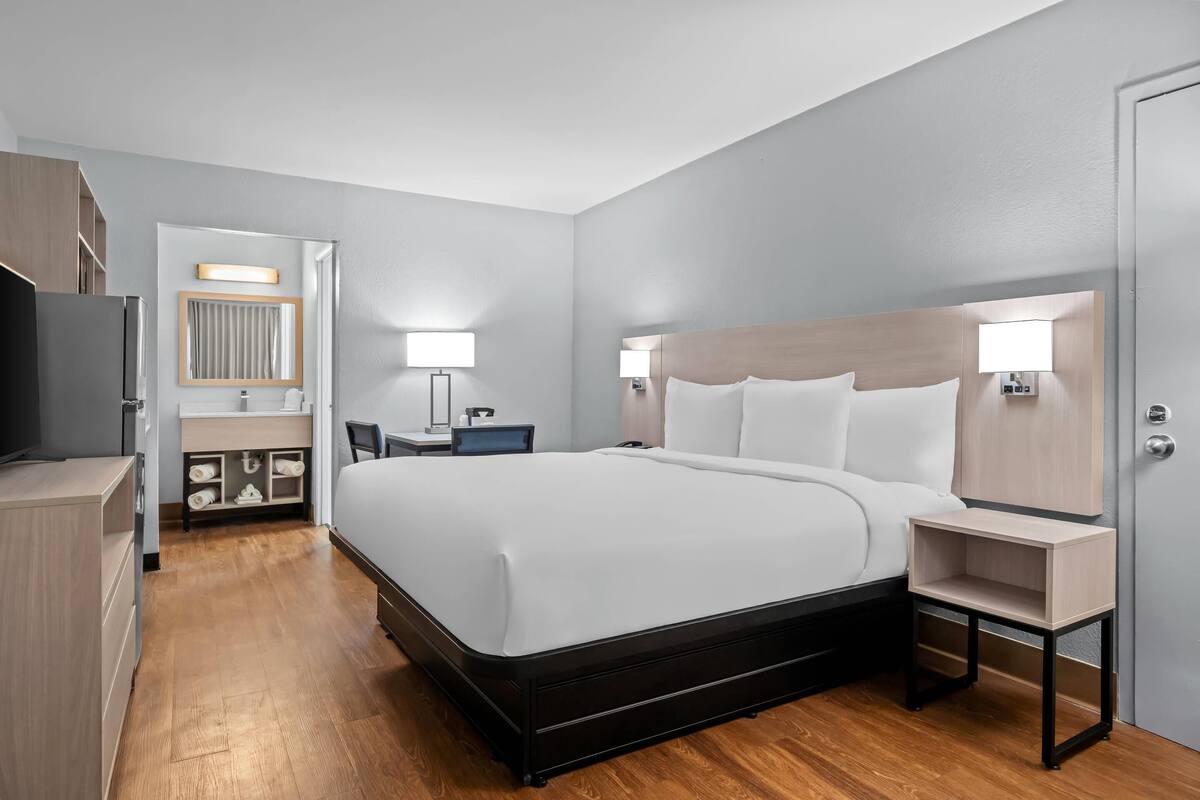 Ein modernes Hotelzimmer mit einem großen Bett, Nachttischen, einem Schreibtisch und einem Spiegel.