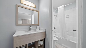 A modern bathroom with a sink, mirror, and shower. - Suburban Studios Daytona Beach - Speedway (Daytona Beach)