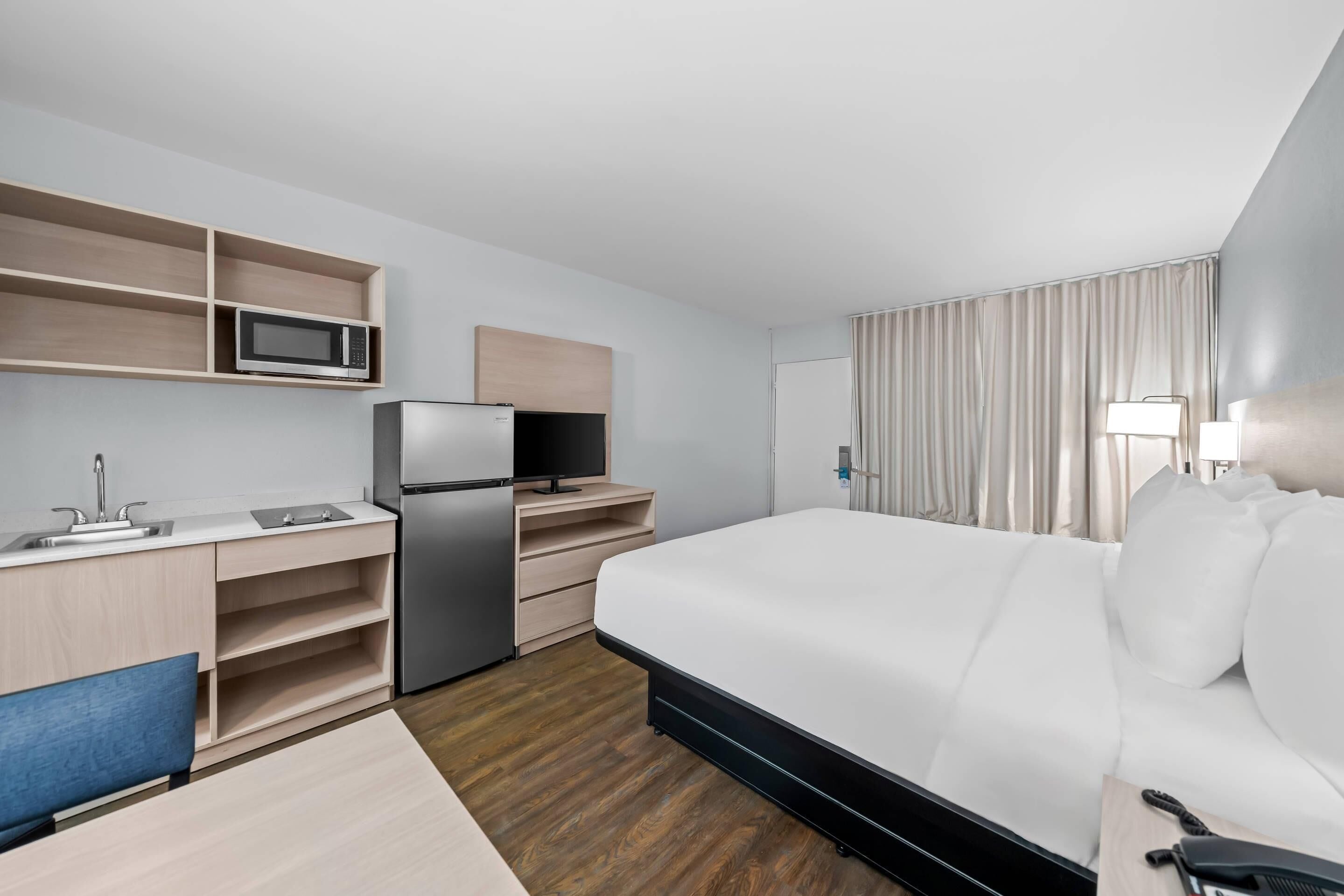 A hotel room with a bed, a desk with a computer, a microwave, and a refrigerator.
