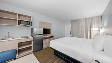 A hotel room with a bed, a desk with a computer, a microwave, and a refrigerator.