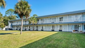 A two-story motel with a flat roof, white exterior, and a covered parking area. - Suburban Studios Daytona Beach - Speedway (Daytona Beach)