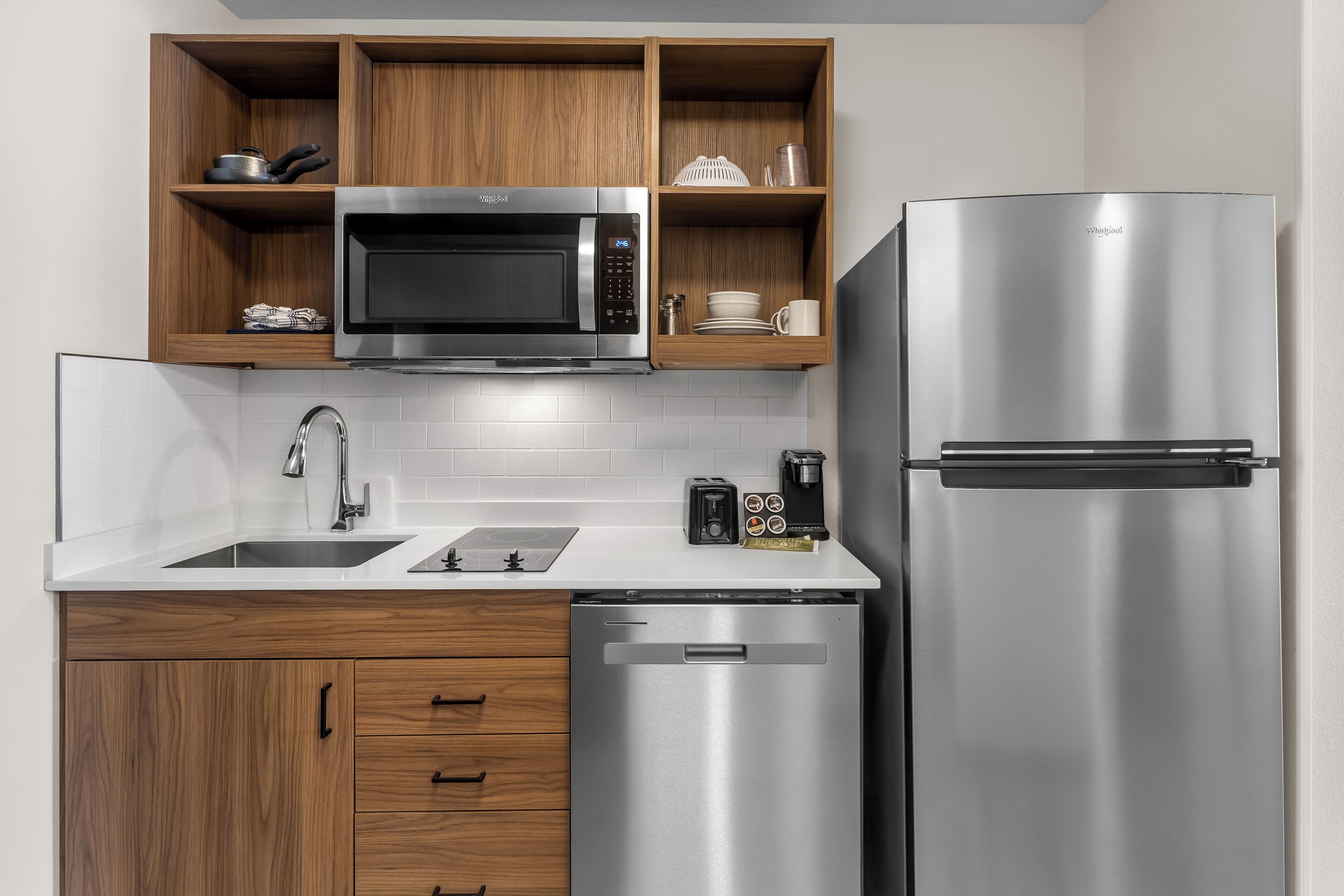 A modern kitchen with a built-in microwave, stainless steel refrigerator, wooden cabinets, a dishwasher, and a coffee maker.