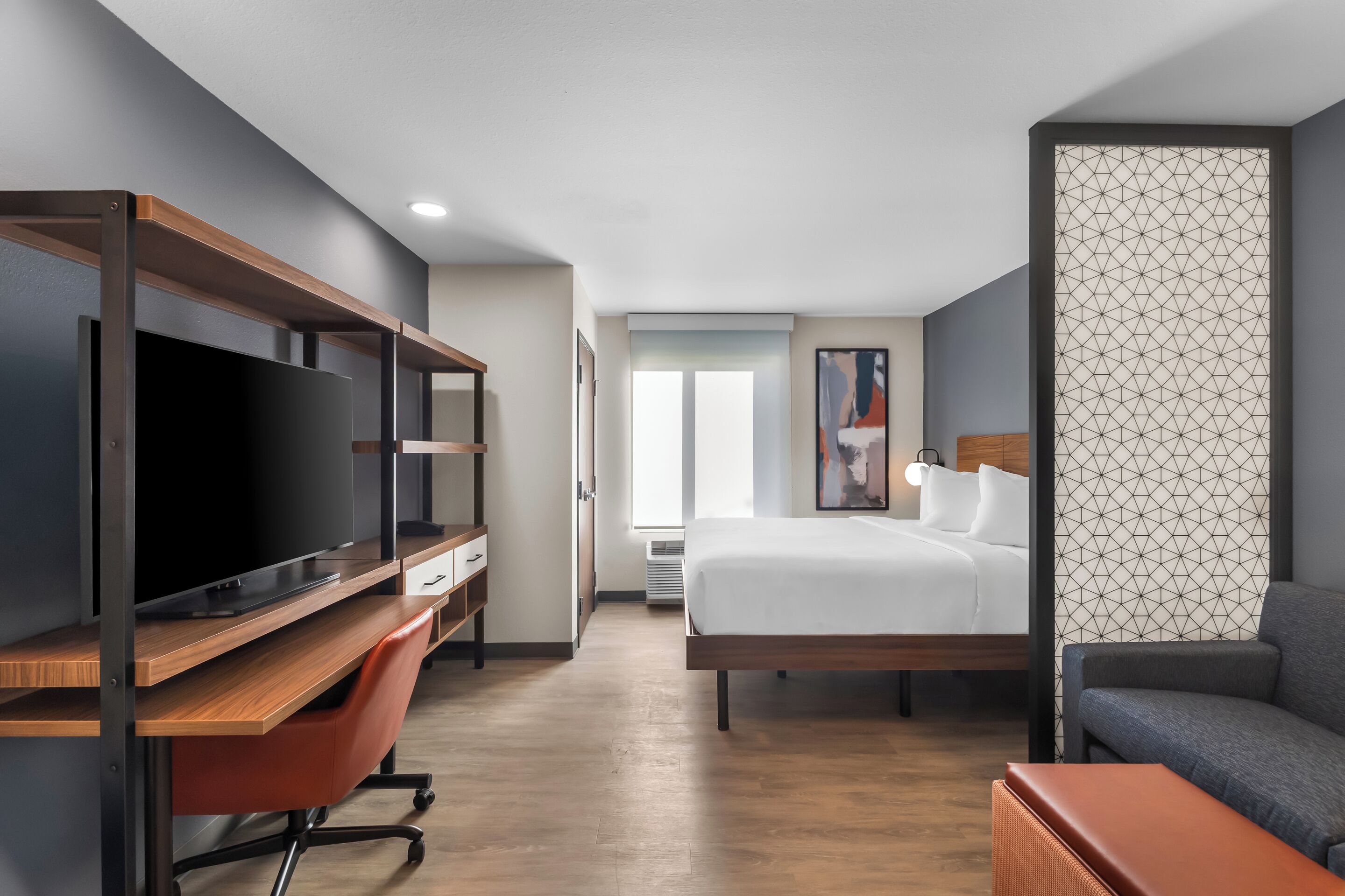 Una habitación de hotel con cama, escritorio con televisor, silla, sofá y ventana.