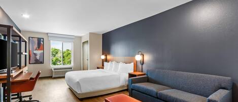 Ett modernt hotellrum med en säng, ett skrivbord, en soffa och en TV.