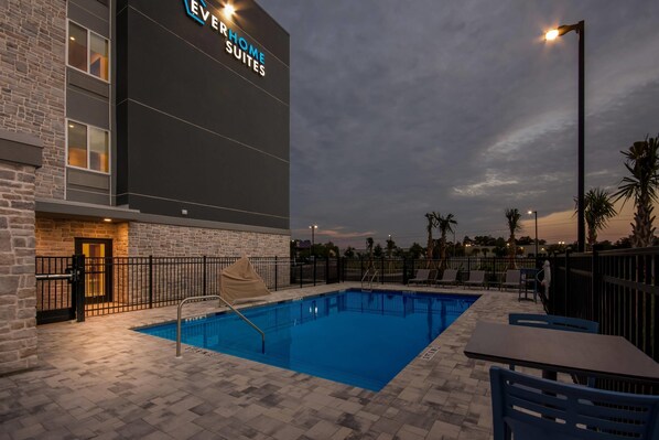 Un hotel con piscina, mobiliario exterior y un cartel grande.