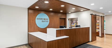 A reception desk with a wooden finish, a circular sign reading 'EVERHOME SUITES,' and a counter with a white top.