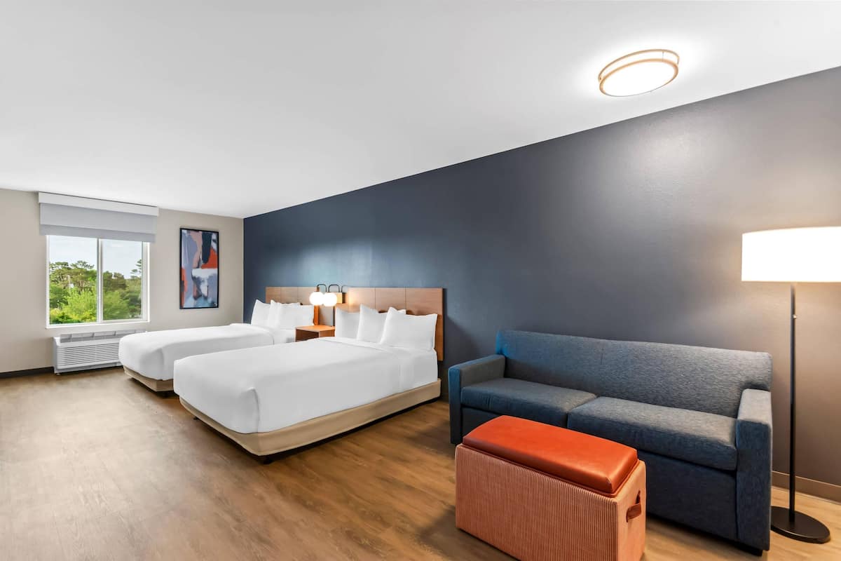 Une chambre d’hôtel avec deux lits, un canapé, une lampe et une fenêtre donnant sur un beau paysage.