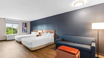 A hotel room with two beds, a sofa, a lamp, and a window with a view.