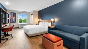 A hotel room with a bed, a desk, a sofa, a small ottoman, and a window with a view.