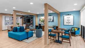 A modern living room with a blue sofa, wooden coffee table, and a dining area with blue chairs.