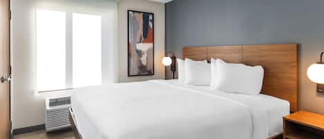 Ein Hotelzimmer mit einem großen Bett, einem Nachttisch, einer Wandlampe, einem Fenster und einer Heizung.