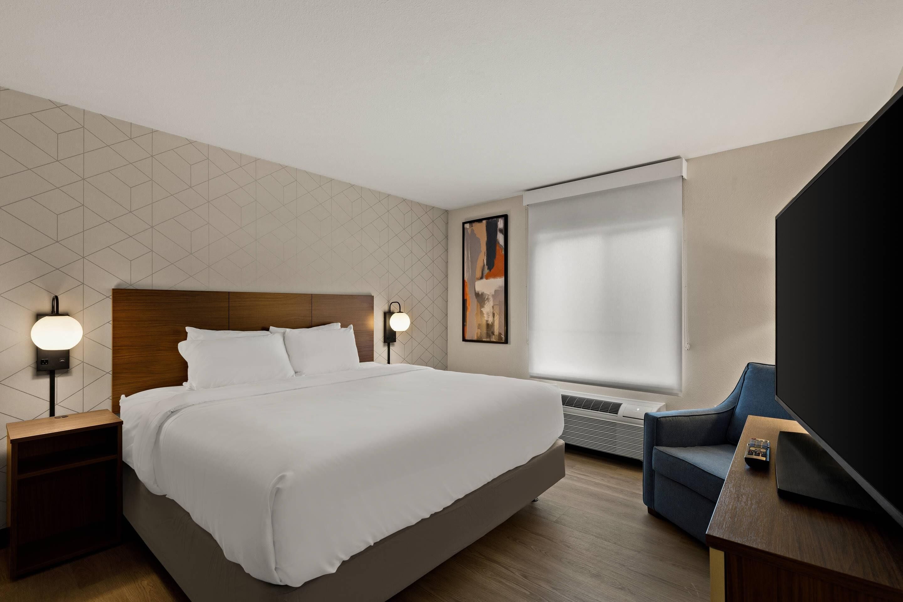 A hotel room with a large bed, a flat-screen TV, a sofa, and a wall-mounted heater.