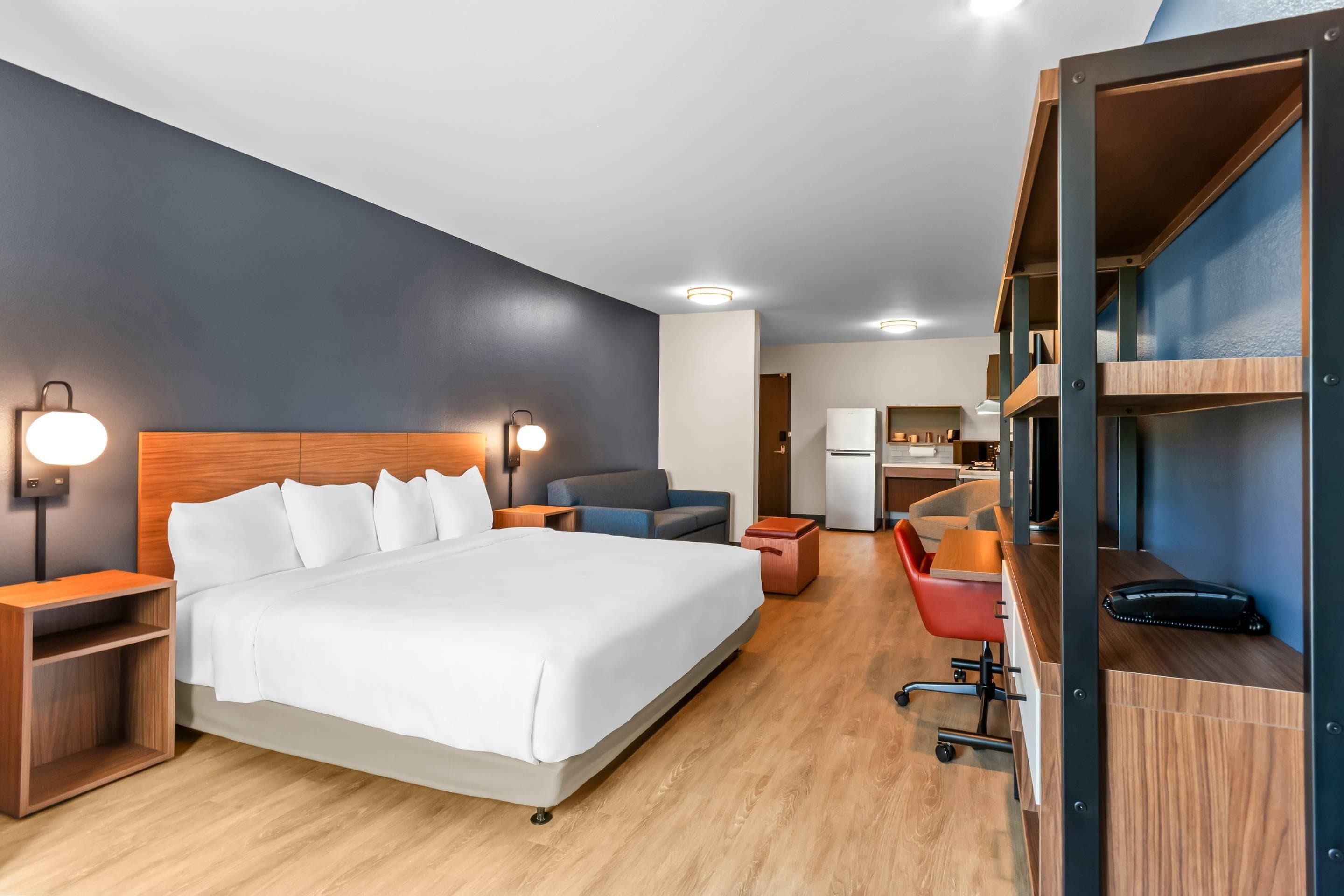 A hotel room with a bed, bedside tables, a desk, a chair, and a kitchenette.