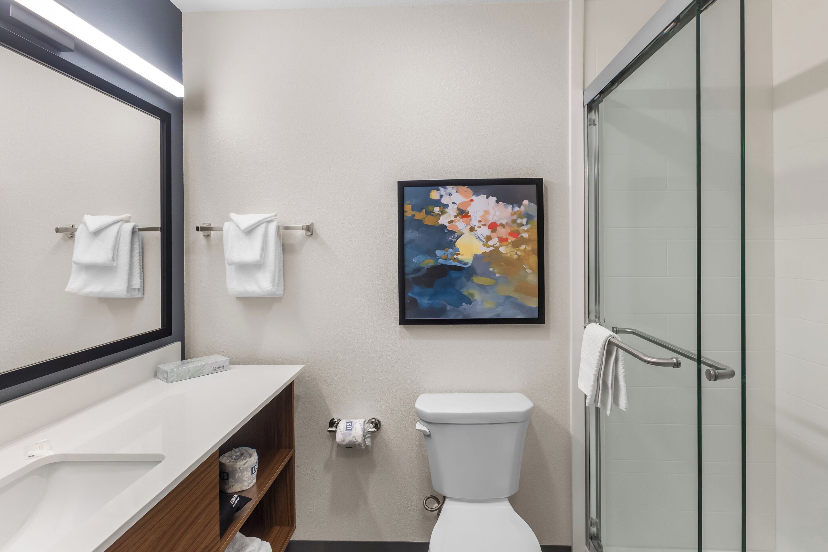 Une salle de bain moderne comprenant des toilettes, une douche en verre, un lavabo avec un miroir et un porte-serviettes.