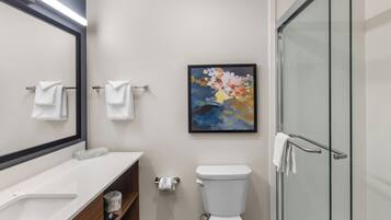 Un baño moderno con inodoro, cabina de ducha de vidrio, lavabo con espejo y toallero.