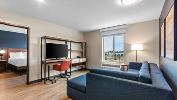 A hotel room with a bed, a desk with a computer, a sofa, a TV, and a window with a view.