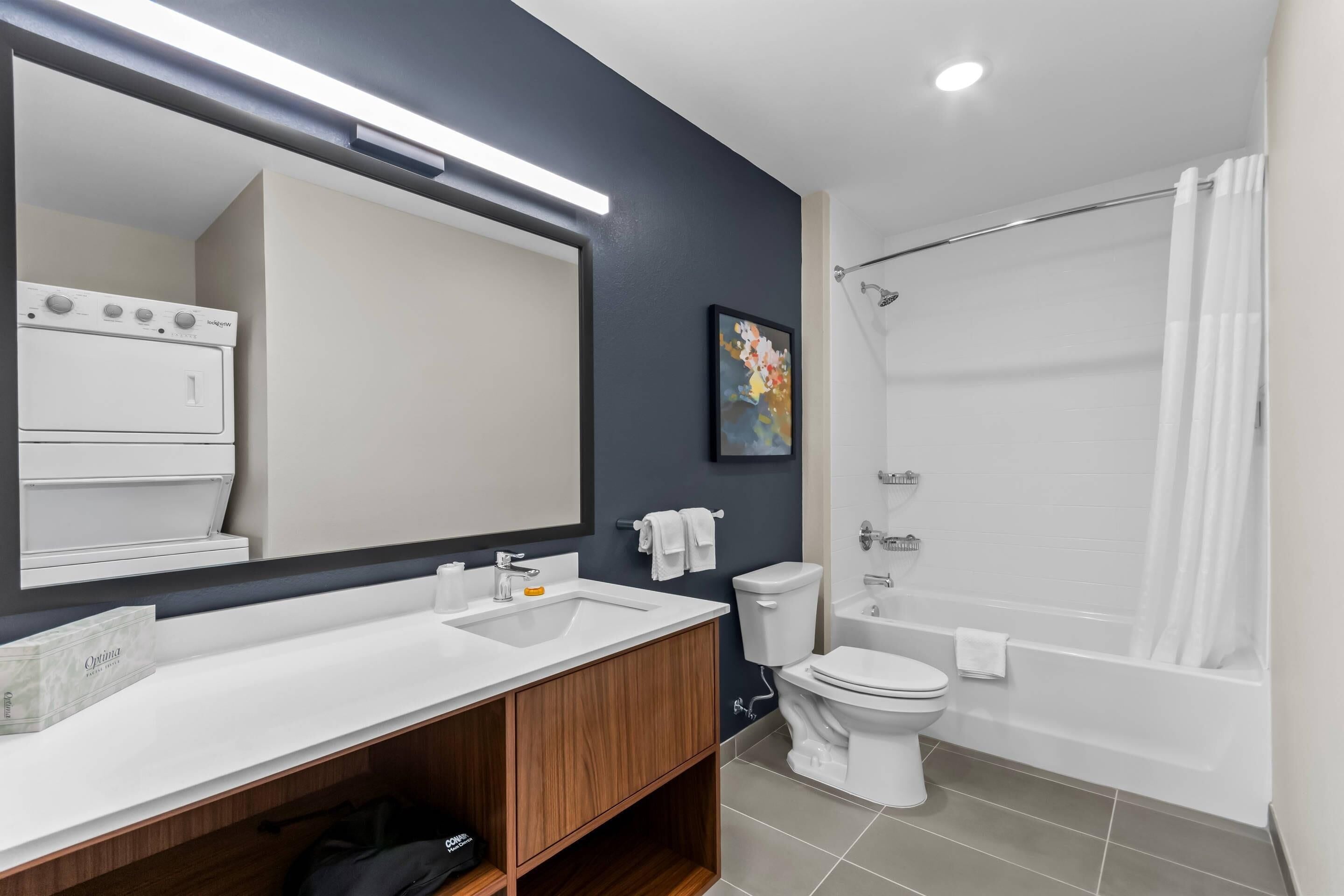 Une salle de bain moderne avec un grand miroir, un lavabo blanc, des toilettes, une baignoire et un rideau de douche.