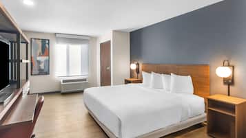 Une chambre d’hôtel avec un grand lit, un bureau, une télévision et une fenêtre avec des stores.