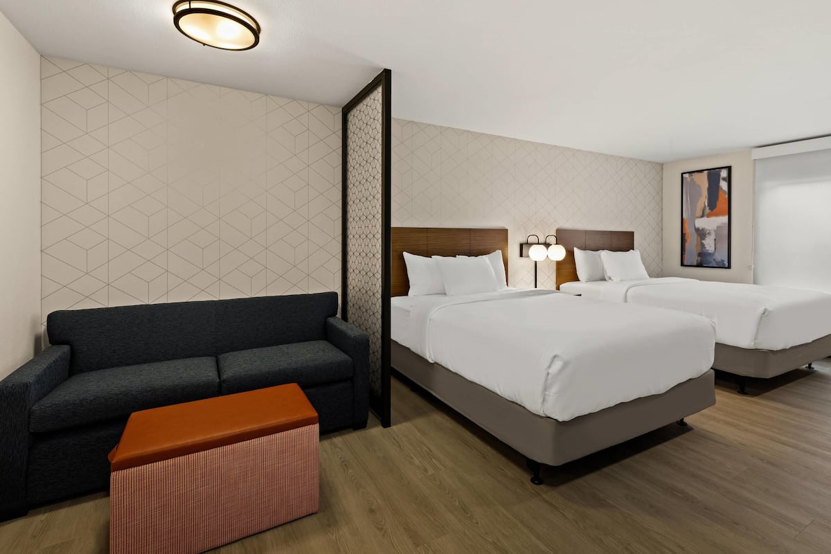 Une chambre d’hôtel avec un canapé, deux lits, un plancher en bois et un mur orné d’un motif géométrique.