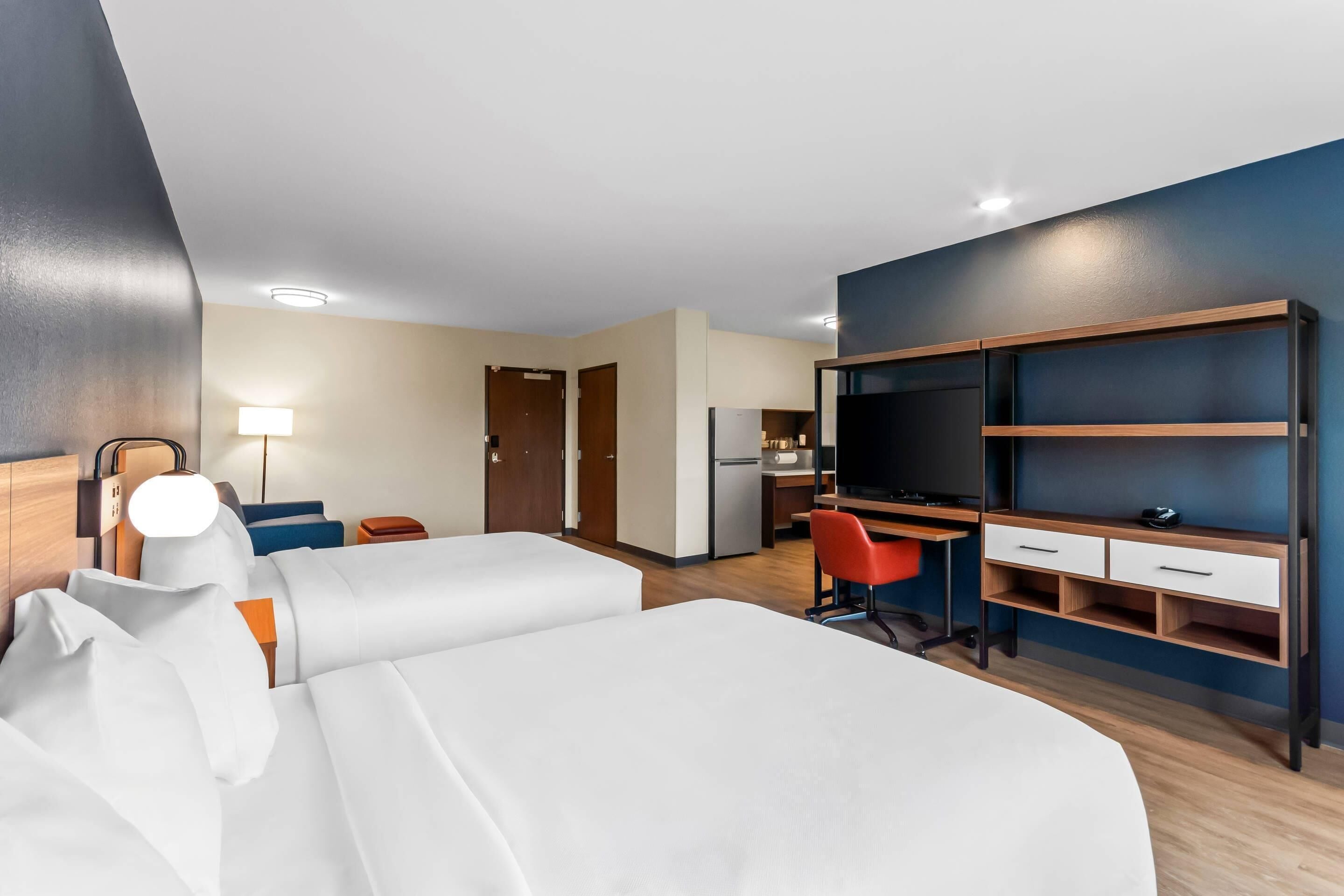 Une chambre d’hôtel avec deux lits, un bureau avec une chaise, une télévision et un mini-bar.