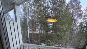A balcony with a white railing, a small table, and a view of trees and a yellow umbrella outside. - Hotell Våler-Elverum-flisa-kirkenær (Våler)