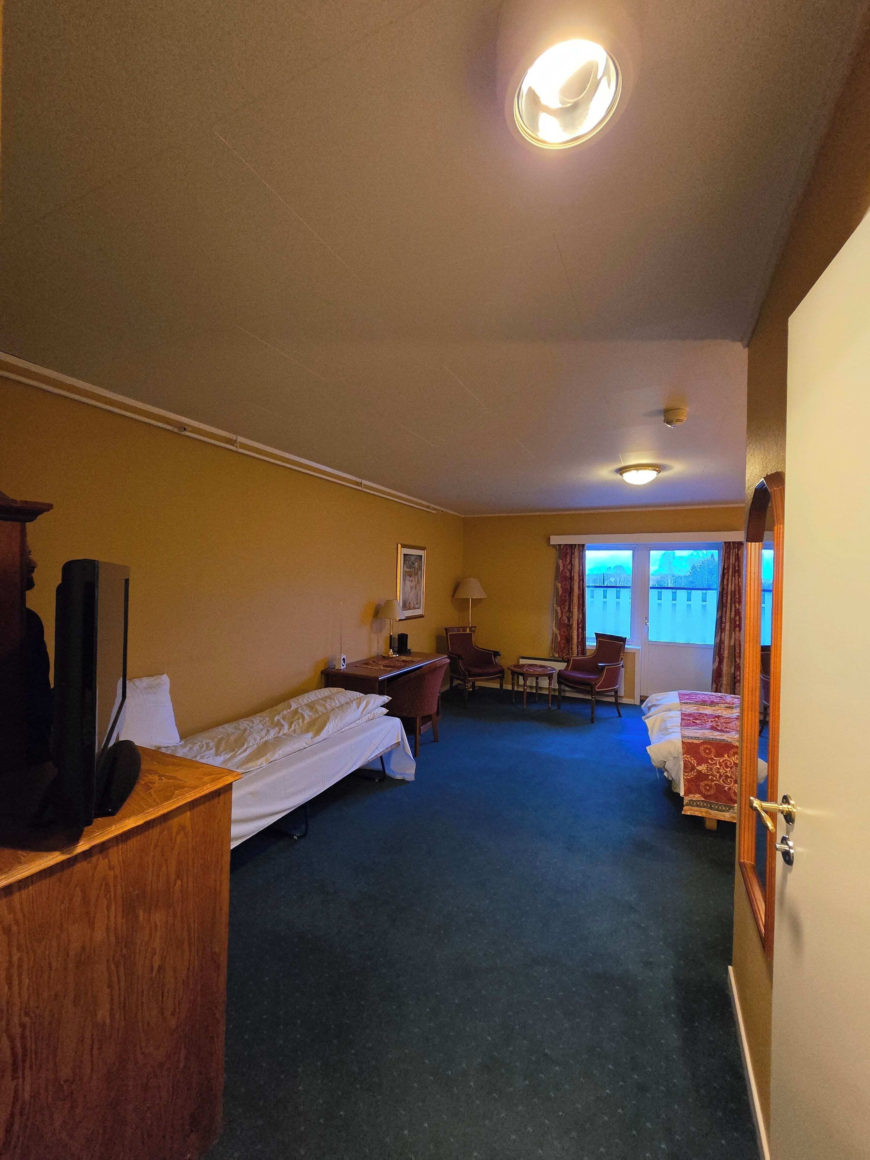 A hotel room with two single beds, a desk, a chair, a television, and a window with a view.