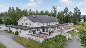 A large, white building with a flat roof and a covered outdoor area with tables and chairs. - Hotell Våler-Elverum-flisa-kirkenær (Våler)
