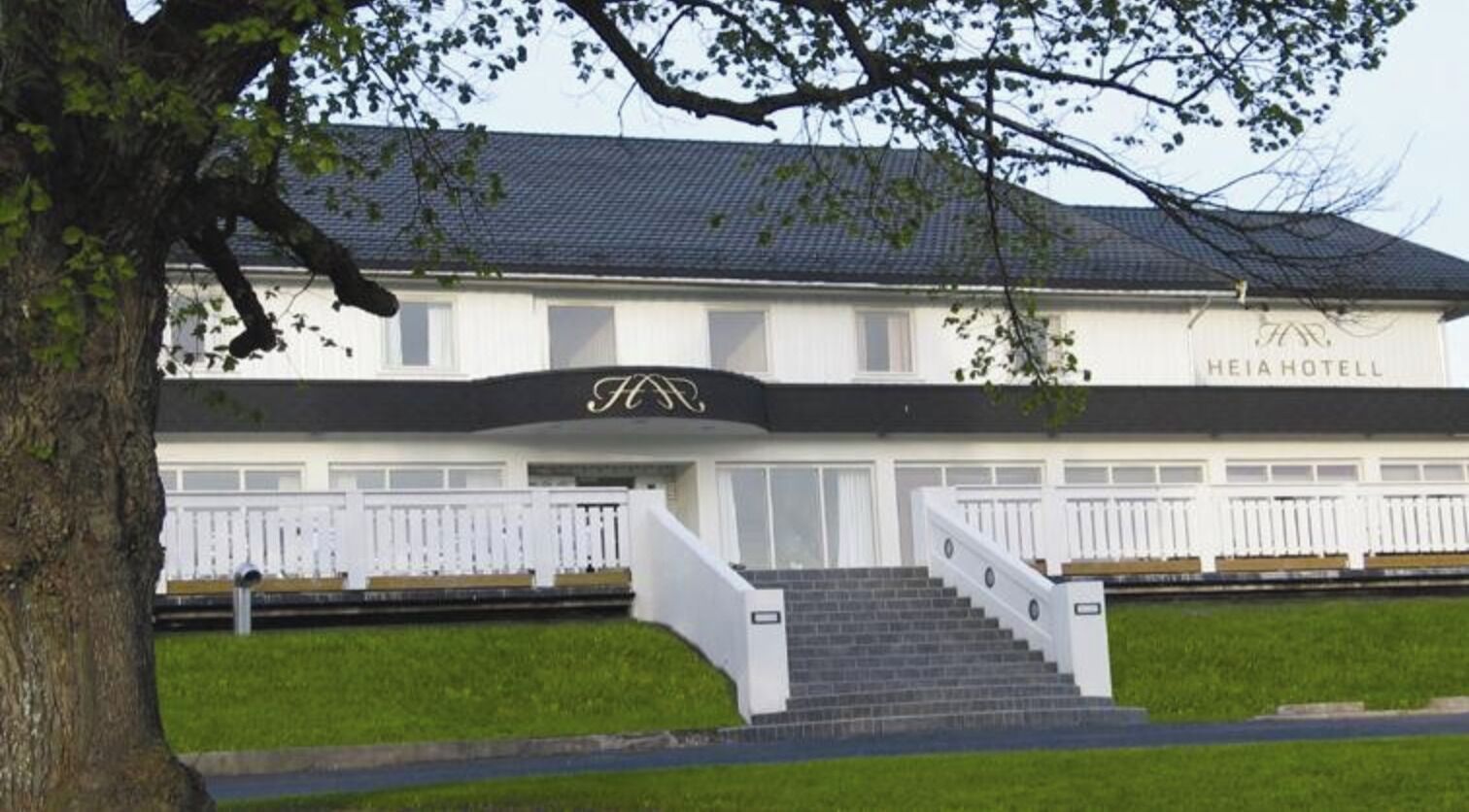 A two-story hotel with a black and white facade, a staircase leading to the entrance, and a white fence surrounding the property.