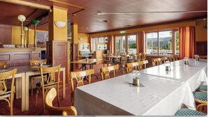 A restaurant with multiple dining tables and chairs, a bar area, and large windows with curtains. - Hotell Våler-Elverum-flisa-kirkenær (Våler)