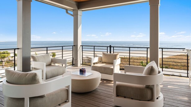 A covered outdoor seating area with white furniture and a view of the ocean.