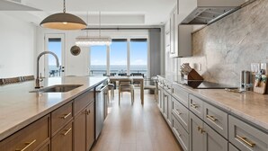 A modern kitchen with a large island, stainless steel appliances, and a view to the outside.